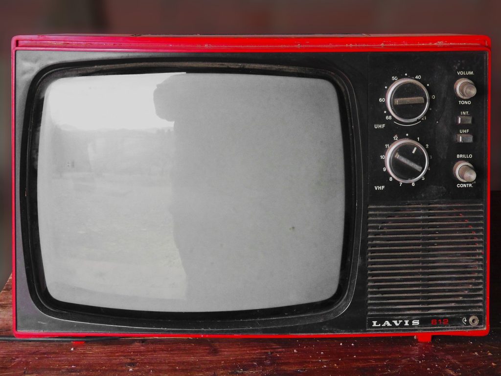 A vintage television. The edges of the set are red, and the screen is off. There are dials on the top right of the set. Christmas TV